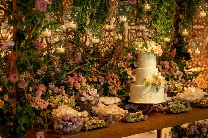 Bolo de dois andares com flores sobre mesa de madeira entre folhagens